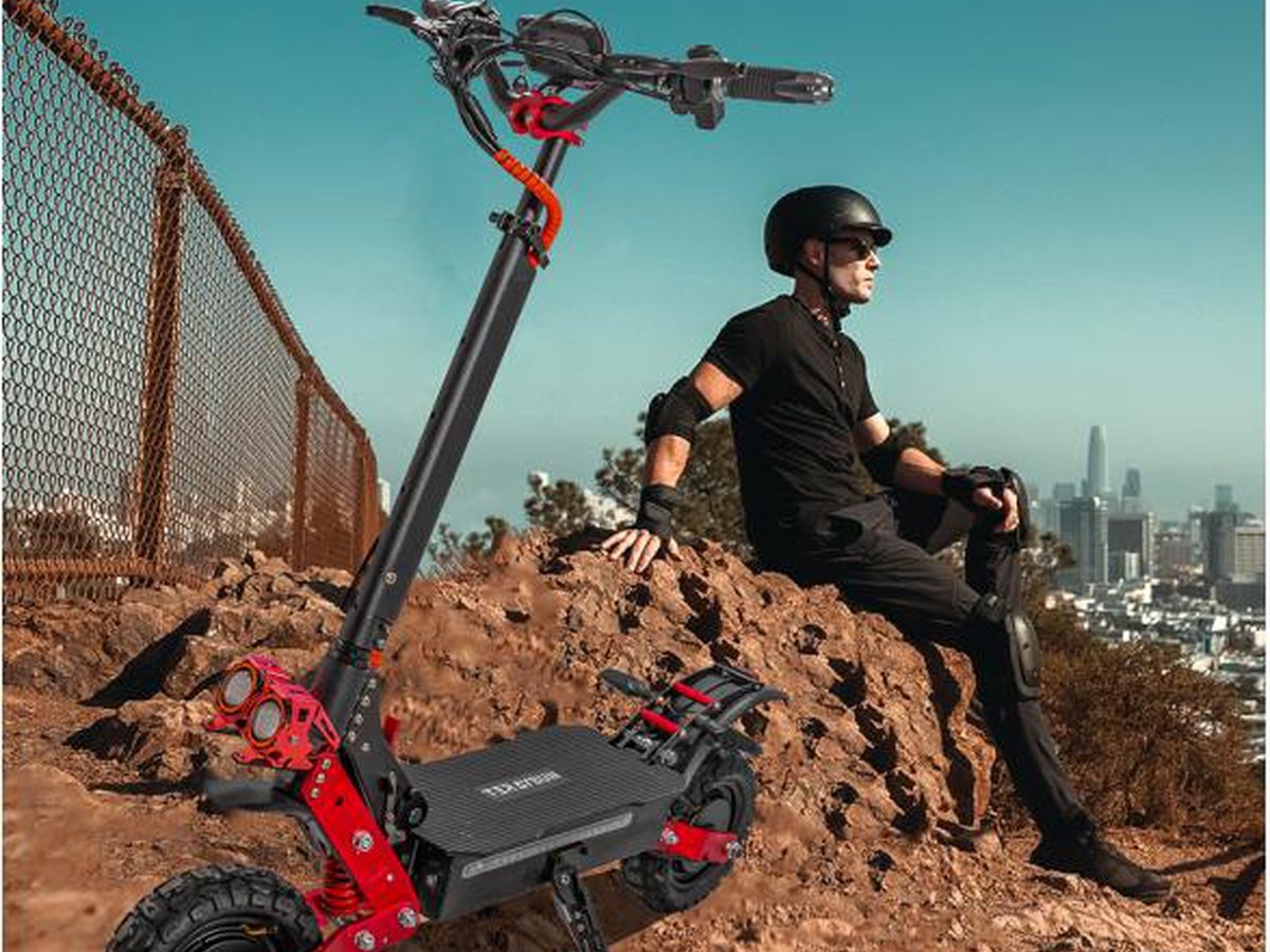 Dual-motor electric scooter on a dirt trail with a city skyline behind