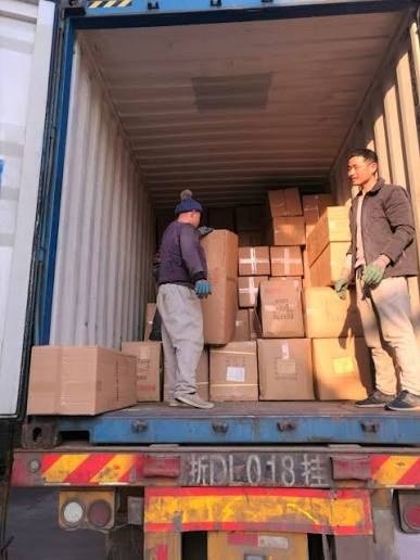 Two workers stacking cartons inside an export container